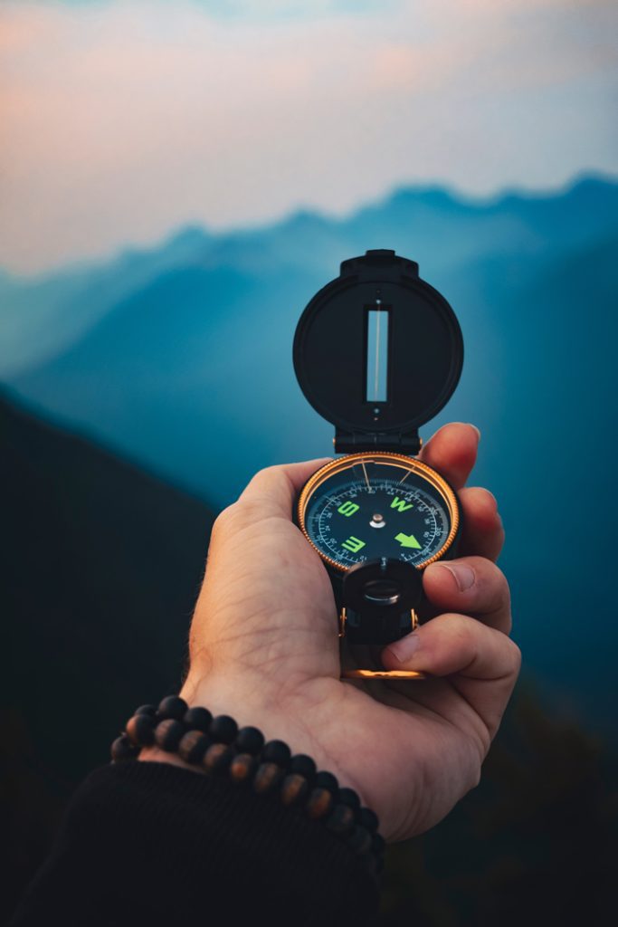 hand holding compass overlooking mountainscape