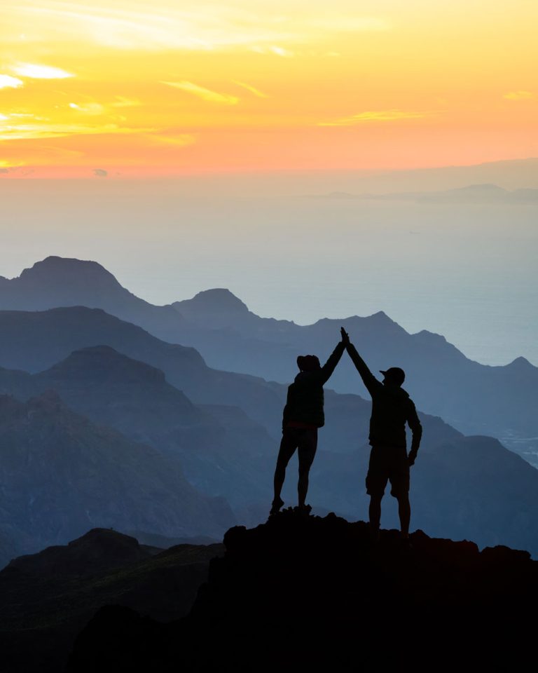 two hikers high-fiving, standing on a mountain