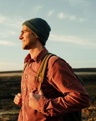 shutterstock_20274379912 youthful male with a brimless hat and a knapsack, facing the sun and smiling.